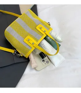 Détail du sac seau tissé jaune montrant un intérieur spacieux avec cosmétiques et mobile