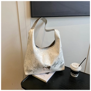 Detail der cremefarbenen Hobo-Bag mit silbernen Schmetterlingsmustern und Metallschnalle
