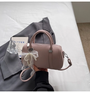 Pink lychee texture leather boston bag with lace pearl bow charm on a grey suit jacket