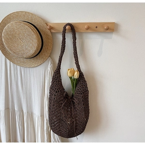 Detail of hollow-out knit tote bag hanging on wooden rack with resort style elements