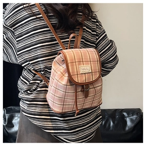 Detail view of a pink plaid canvas backpack with leather straps on a female model