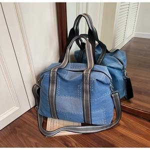 Detail of blue denim tote bag with white contrast stitching and striped webbing handles