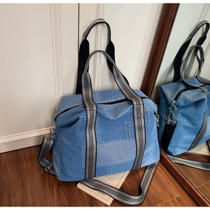 Detailed view of large denim tote bag with white stitching and striped webbing handles