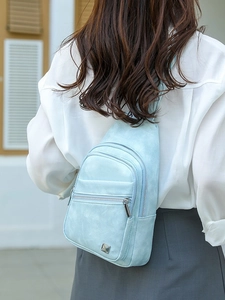 Light blue textured crossbody chest bag with silver zipper on an urban outdoor model