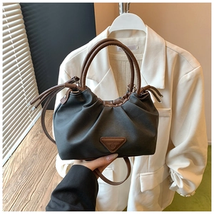 Detailed view of dark grey pleated handbag with brown leather handles and a triangle patch