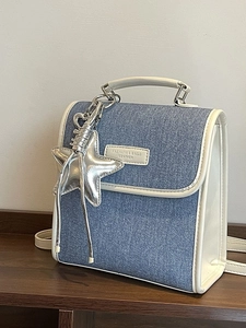 Chic blue denim and cream leather handbag with star charm on dark wood background