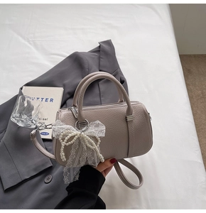 Detail of greyish-purple litchi leather texture with pearl lace bow charm on handbag