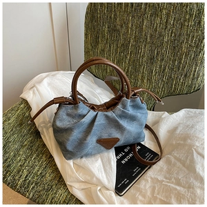 Detail of blue denim bucket bag with brown leather trim and drawstring closure on chair