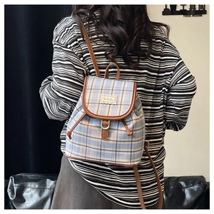 Detail showing vintage plaid canvas backpack with brown leather trim and drawstring cover