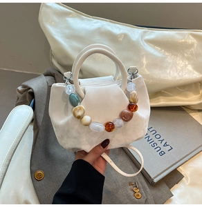 Détail d'un sac seau plissé blanc avec poignée en perles résine et bandoulière amovible
