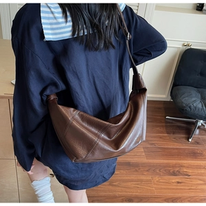 Detail view of glossy dark brown crescent bag with adjustable strap on a model