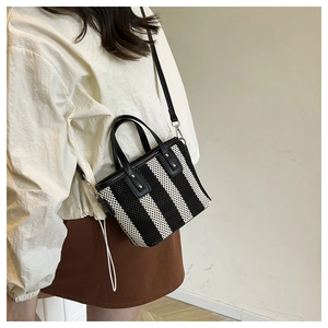 Détail d'un sac seau tissé à rayures noires et blanches avec poignées en cuir et rivets