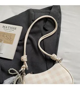 Détail du sac baguette à carreaux avec breloque perle et bandoulière nouée sur un livre d'art