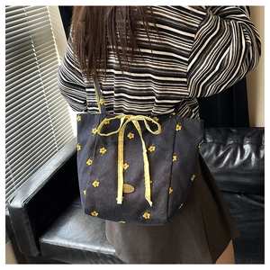 Detail of navy canvas tote with yellow floral embroidery and a plaid bow decoration