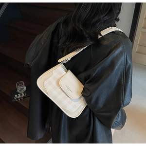 Detail of a beige textured crossbody bag with flap and adjustable strap on a woman