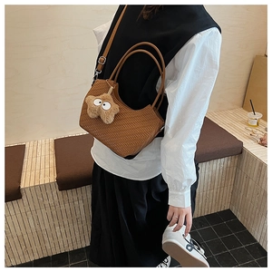 Détail d'un sac cabas tressé marron avec un pendentif en peluche étoile et bandoulière