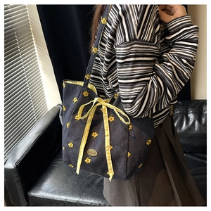 Detail of navy canvas tote bag featuring yellow floral embroidery and checkered bow accent