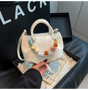 Détail du sac seau plissé blanc avec poignée en perles colorées dans un coffret