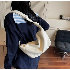 Detail of cream oversized dumpling bag featuring matte pleated texture and knotted strap