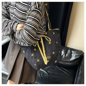 Detail of dark blue canvas tote bag featuring yellow floral embroidery and ribbon