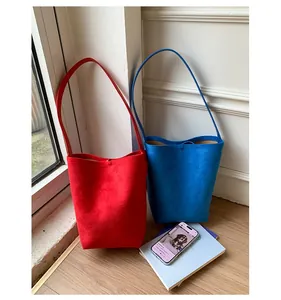Detail of minimalist suede bucket bags in vibrant red and blue colors on a wooden surface