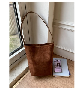 Detail of dark caramel suede bucket bag with slim shoulder strap on wooden surface