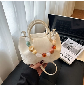 Détail du sac seau crème avec poignée ornée de perles de résine ambre et vert forêt
