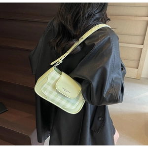 Detail view of the green checkered crossbody bag on a model in a black leather jacket