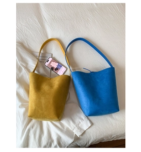 Top view of yellow and blue matte bucket bags on a white bed with accessories