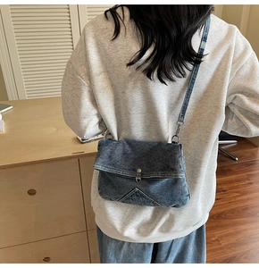 Detailed view of a vintage denim crossbody bag with flap and metal snap on a model