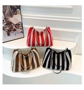 Close-up of three striped knit tote bags with leather chain straps on a white display