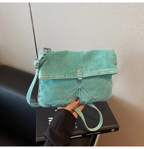 Detail of mint green denim crossbody bag showing metal button and V-shaped stitching