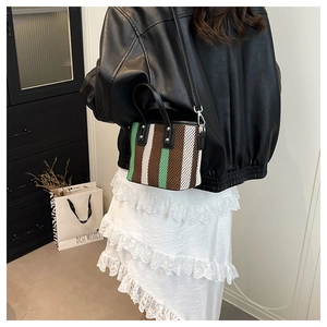 Détail d'un sac seau tressé avec des rayures vertes, blanches, brunes et une bandoulière en cuir