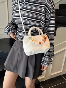 Sac seau blanc plissé avec perles colorées porté par un mannequin dans un décor moderne