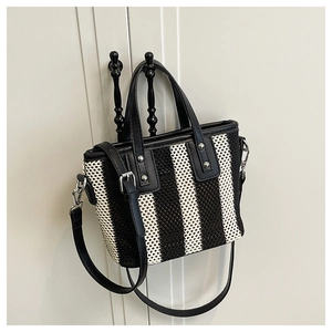 Détail du sac seau tissé noir et blanc montrant les poignées en similicuir et les boucles