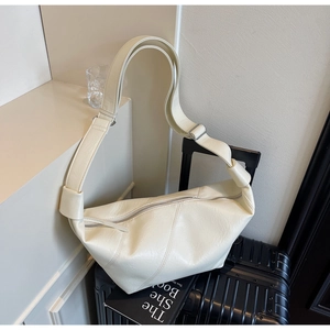 Close-up of a cream croissant shoulder bag with knotted strap on a black suitcase