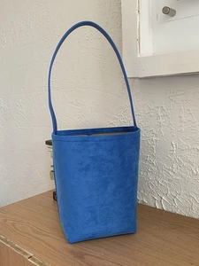 Blue suede bucket shoulder bag with minimalist design on light wooden table