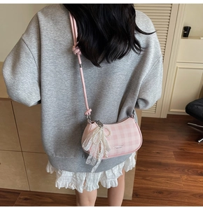 Sac sous le bras à carreaux roses avec breloque nœud en dentelle porté par un modèle