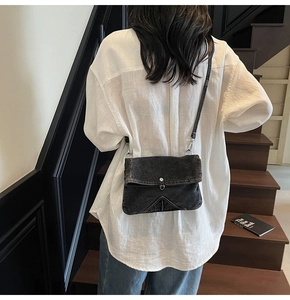 Close-up of vintage black denim crossbody bag with V-shaped stitching and metal buckle