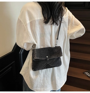 Detail of vintage black denim crossbody bag with V-shaped stitching on the flap cover
