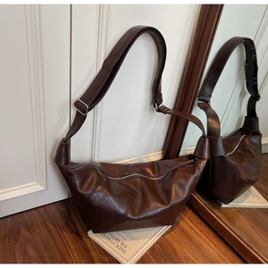 Detail of dark brown leather crescent bag with wrinkled texture and wide shoulder strap