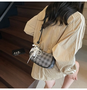 Détail d'un sac à carreaux avec nœud en dentelle et breloque perle porté par un modèle