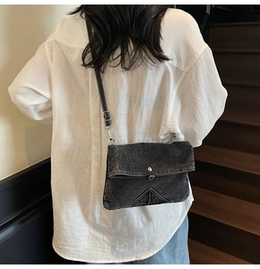 Detail of black denim crossbody bag featuring white contrast stitching and silver buckle