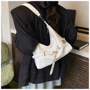 White patent leather hobo bag with silver buckle strap shown in a lifestyle street setting