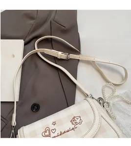 Detail of checkered crossbody bag with heart print next to pearls and lace charms