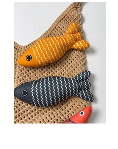 Detailed close-up of fish-shaped fabric cat toys on a beige woven mesh tote bag