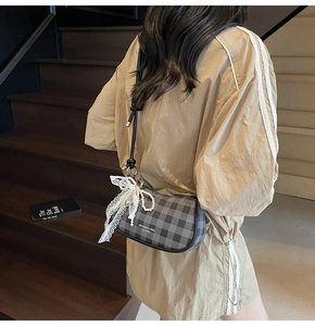 Détail du sac hobo à carreaux gris avec nœud en dentelle et chaîne de perles sur escalier