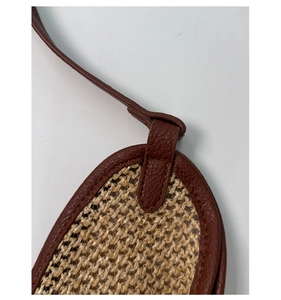 Detailed stitching of dark brown leather straps on a beige straw bucket beach bag