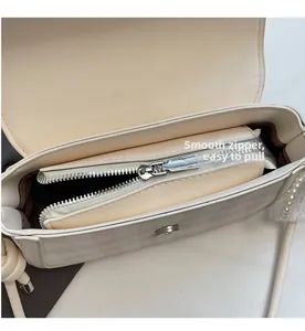 Detail of beige shoulder bag interior featuring smooth silver zipper and pearl chain strap
