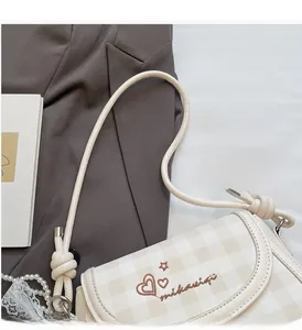 Detail view of cream plaid baguette bag with embroidery and knotted strap accents